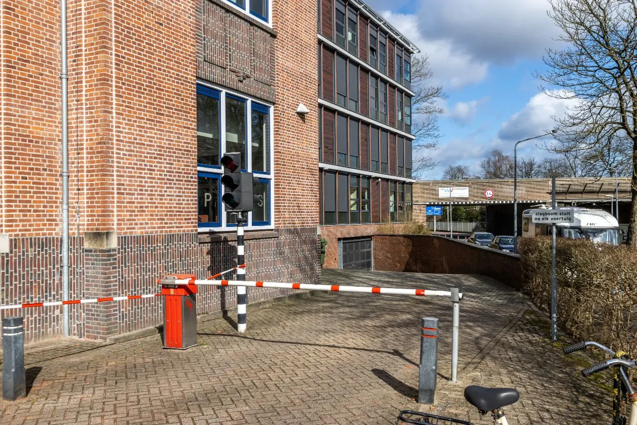 Ingang van een ondergrondse parkeergarage aan de Lage Naarderweg, met slagboom, verkeerslicht en omringende kantoorgebouwen.